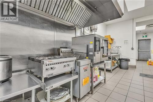Industrial kitchen featuring stainless steel countertops, a commercial range with overhead ventilation, and tiled flooring - 5 Manitou Drive Unit# 106B, Kitchener, ON 