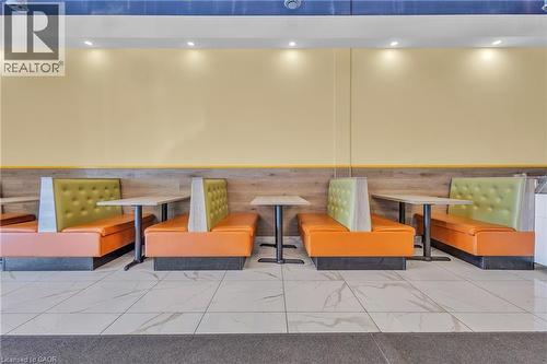 Banquette seating with orange and olive green upholstery, complemented by light wood-finish wall paneling and a cream-colored wall - 5 Manitou Drive Unit# 106B, Kitchener, ON 