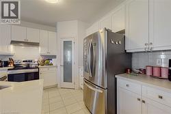 Kitchen featuring white cabinetry, light-toned countertops, tile flooring, stainless steel appliances, and a glass-paneled pantry door - 