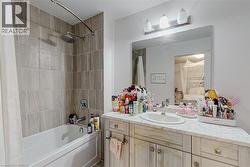 Bathroom featuring a large vanity with a single basin, a marble-finish countertop, and light wood-finish cabinetry with brass-tone hardware - 