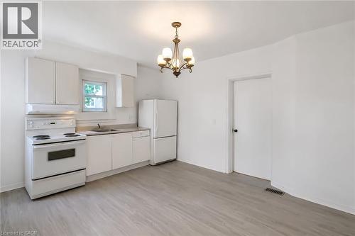 Kitchen space featuring a white appliance suite, light wood-finish flooring, and a classic chandelier - 87 Lancaster Street W, Kitchener, ON - Indoor Photo Showing Kitchen