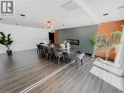 Spacious room featuring wood-finish flooring, a contemporary fireplace within a dark panel wall, and an exposed brick accent wall - 