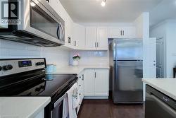 Modern kitchen featuring white shaker cabinetry with dark hardware, white subway tile backsplash, and stainless steel appliances including an over-range microwave, electric range, and refrigerator - 