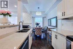 Modern kitchen featuring a double basin undermount sink with a gooseneck faucet, light-toned countertops, and crisp white cabinetry with matte black hardware - 