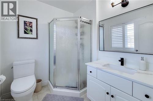 Bathroom featuring a corner shower with frosted glass enclosure, a vanity with a white countertop and integrated sink, white cabinetry with dark hardware, a rectangular framed mirror, and a wall-mount - 232 Stonehenge Drive Unit# 2, Ancaster, ON - Indoor Photo Showing Bathroom