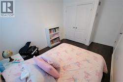 Spacious room featuring wood-finish flooring, white baseboards, and a built-in double-door closet with paneling - 
