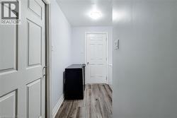 Hallway featuring wood-finish flooring, white paneled doors, and contemporary overhead lighting - 