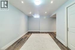 Spacious room featuring wood-finish flooring, light blue walls, recessed lighting, a ceiling-mounted light fixture, and a white two-panel door with a brushed metal handle - 