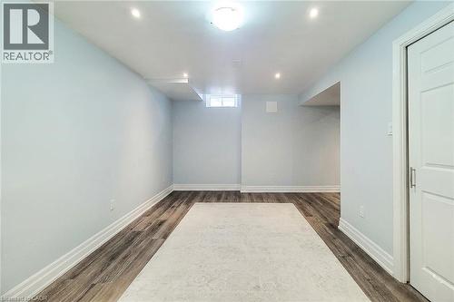 Spacious room featuring wood-finish flooring, light blue walls, recessed lighting, a ceiling-mounted light fixture, and a white two-panel door with a brushed metal handle - 232 Stonehenge Drive Unit# 2, Ancaster, ON - Indoor