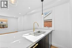 Kitchen with light wood finished floors, light stone countertops, dishwasher, hanging light fixtures, and dark cabinetry - 