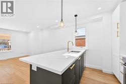 Kitchen with a peninsula, hanging light fixtures, light wood-type flooring, light stone counters, and two tone color scheme - 