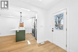 Dual tone kitchen with hanging light fixtures, light wood-style floors, a kitchen breakfast bar, a center island with sink, and stainless steel appliances - 