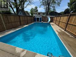 In-ground swimming pool with a concrete surround, wood privacy fencing, and an adjacent storage shed - 
