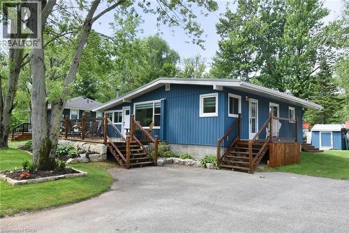 Exterior featuring blue vertical panel siding, white trim windows, two wooden staircases with black metal railings, a paved driveway, and a detached shed - 5 Ralph Street, Turkey Point, ON - Outdoor With Deck Patio Veranda