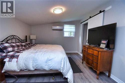 Bedroom featuring wood-finish flooring, a wall-mounted mini-split unit, a window with blinds, a ceiling-mounted light fixture, and a white barn door on a black track - 5 Ralph Street, Turkey Point, ON - Indoor Photo Showing Bedroom