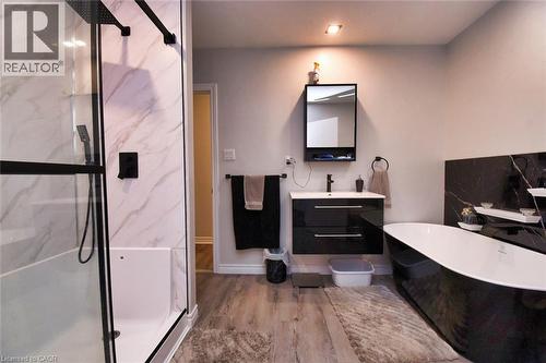 Modern bathroom featuring a black-framed glass shower enclosure with a rainfall showerhead, a freestanding black and white soaking tub, a black vanity with a white countertop and basin, wood-finish fl - 5 Ralph Street, Turkey Point, ON - Indoor Photo Showing Bathroom