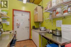 Commercial kitchen space featuring a walk-in cooler, stainless steel workstations, tiled flooring, wood-finish upper cabinetry, and wire shelving - 