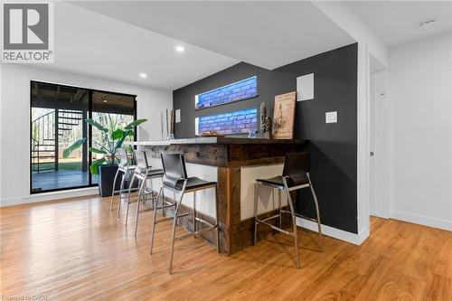 Entertainment area featuring wood-finish flooring, a built-in bar with a stone countertop, and brick-textured wall accents with integrated lighting - 39 Hilts Drive, Stoney Creek, ON - Indoor Photo Showing Dining Room