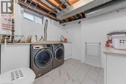 Dedicated laundry area featuring white tile flooring, white cabinetry, integrated sink, and exposed ceiling joists - 
