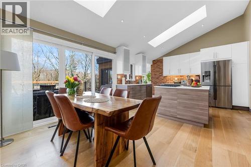 Open-concept living space featuring wood-finish flooring, a vaulted ceiling with skylights, extensive sliding glass doors, a kitchen island with integrated cooktop, and a brick accent wall - 39 Hilts Drive, Stoney Creek, ON - Indoor Photo Showing Other Room