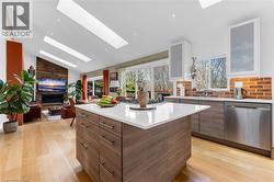 Open-concept living space featuring a central kitchen island with a white countertop, light wood-finish flooring, and a brick-finish backsplash - 