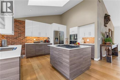 Open-concept kitchen featuring an expansive center island with gas cooktop, sleek stainless steel appliances, brick-finish backsplash, wood-finish flooring, and a skylight - 39 Hilts Drive, Stoney Creek, ON - Indoor Photo Showing Kitchen With Upgraded Kitchen
