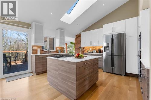 Modern kitchen featuring wood-finish flooring, a central island with a cooktop, white upper cabinetry, and wood-finish lower cabinetry - 39 Hilts Drive, Stoney Creek, ON - Indoor Photo Showing Kitchen