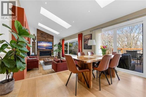 Vaulted ceilings with multiple skylights, light wood-finish flooring, and a natural wood accent wall featuring a built-in fireplace - 39 Hilts Drive, Stoney Creek, ON - Indoor Photo Showing Dining Room With Fireplace