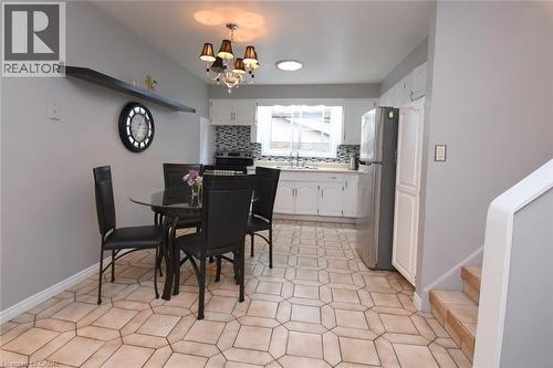 Open-concept kitchen and dining area featuring geometric tile flooring, white cabinetry, a tiled backsplash, and an overhead chandelier with decorative accents - 64 Winnett Street N, Cayuga, ON 