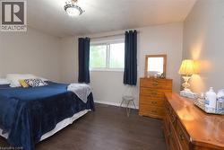 Spacious room featuring wood-finish flooring, a large window with privacy curtains, and neutral wall tones - 