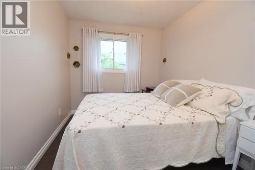 Bedroom featuring a window with white window treatments, dark wood-finish flooring, white baseboards, and light neutral wall paint - 64 Winnett Street N, Cayuga, ON 