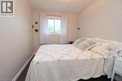 Bedroom featuring a window with white window treatments, dark wood-finish flooring, white baseboards, and light neutral wall paint - 