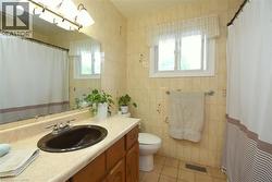 Bathroom featuring a wood-finish vanity with an oval sink, an overhead light fixture, and a large wall-mounted mirror - 