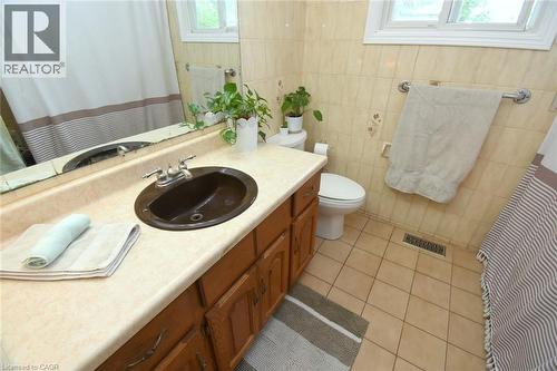 Bathroom featuring a single-basin vanity with a light-toned countertop, wood cabinetry, and a dark oval sink - 64 Winnett Street N, Cayuga, ON 
