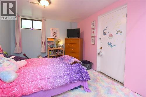 Bedroom featuring a window with natural light, light blue and pink painted walls, a flush-mount ceiling light fixture, and a white door with decorative accents - 64 Winnett Street N, Cayuga, ON 
