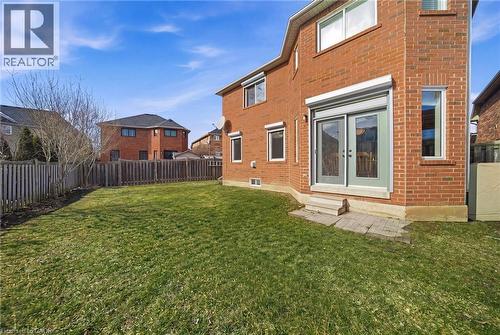 Expansive backyard featuring a manicured lawn, full perimeter fencing, brick exterior, and a patio door with exterior roller shutter - 2070 Willhaven Trail, Oakville, ON - Outdoor With Exterior