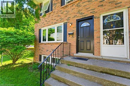 Brick exterior featuring a black paneled door with an arched window, white-framed windows, and black louvered shutters - 26 Coachwood Road Unit# 6, Brantford, ON - Outdoor With Exterior