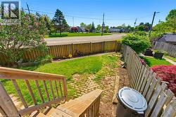 Exterior staircase with wood railing descends to a fenced yard featuring a grass lawn, brick paver patio area, and mature foliage - 