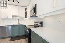 Modern kitchen featuring two-tone cabinetry with white upper cabinets and sage green lower cabinets, stainless steel appliances, white countertops, and a gold-tone faucet - 