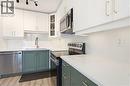 Modern kitchen featuring two-tone cabinetry with white upper cabinets and sage green lower cabinets, stainless steel appliances, white countertops, and a gold-tone faucet - 26 Coachwood Road Unit# 6, Brantford, ON  - Indoor Photo Showing Kitchen 