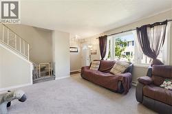 Carpeted living area featuring a large window, light beige wall paint, white trim, and a white front entry door with a half-moon window - 
