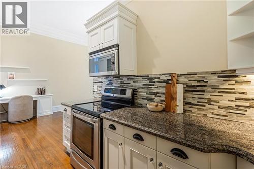 Kitchen featuring stainless steel appliances, open shelves, dark stone countertops, dark wood-style flooring, and crown molding - 46 Herkimer Street Unit# 2, Hamilton, ON - Indoor Photo Showing Kitchen