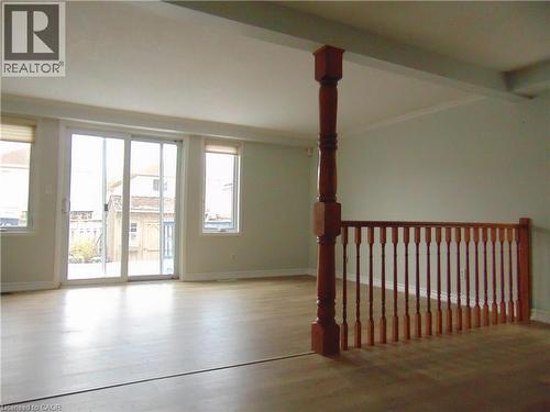 Light wood-finish flooring throughout, featuring a sliding glass door with two flanking windows, crown molding, and a warm wood baluster and railing system - 90 Bridlewreath Street Unit# Upper Unit, Kitchener, ON - Indoor Photo Showing Other Room