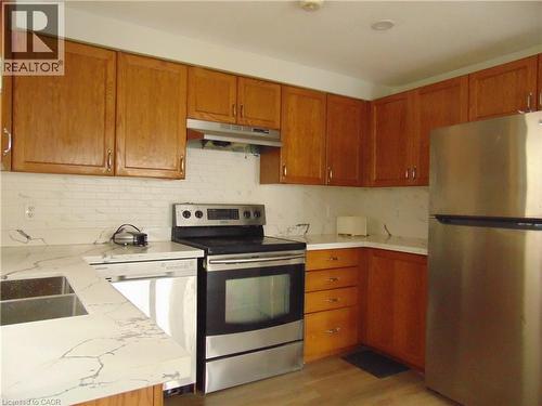 Kitchen featuring wood cabinetry, white marble-look countertops, white subway tile backsplash, and stainless steel appliances including a refrigerator, range, and dishwasher - 90 Bridlewreath Street Unit# Upper Unit, Kitchener, ON - Indoor Photo Showing Kitchen With Double Sink