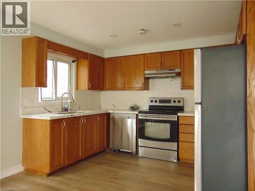 L-shaped kitchen with wood-finish cabinetry, light-toned countertops, and a white tile backsplash - 90 Bridlewreath Street Unit# Upper Unit, Kitchener, ON - Indoor Photo Showing Kitchen