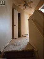 Hallway area featuring a ceiling fan with light kit, baseboard heating, and an open doorway - 