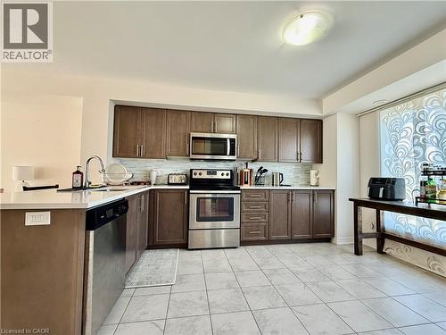 Kitchen featuring wood-finish cabinetry, stainless steel appliances, a white solid surface countertop, a tile backsplash, and light-toned tile flooring - 146 Watson Parkway, Guelph, ON - Indoor Photo Showing Kitchen With Stainless Steel Kitchen