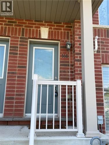 Brick facade entry featuring a grey paneled door with glass insert, white railing, exterior wall lantern, and concrete porch - 146 Watson Parkway, Guelph, ON - Outdoor