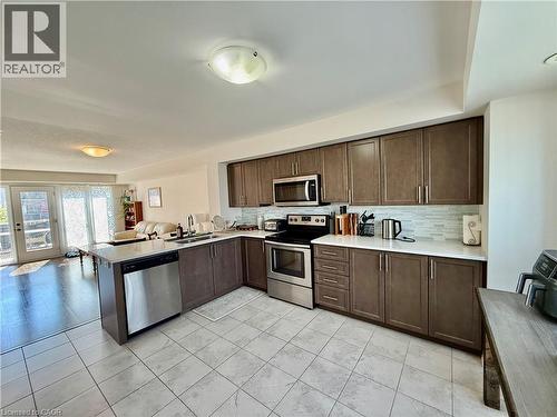 Open-concept kitchen featuring wood-finish cabinetry, stainless steel appliances, white countertops, a tile backsplash, and tile flooring - 146 Watson Parkway, Guelph, ON - Indoor Photo Showing Kitchen With Double Sink
