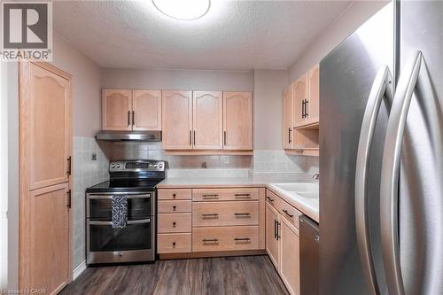 Kitchen featuring light wood cabinetry, stainless steel appliances, a tile backsplash, and wood-finish flooring - 500 Green Road Unit# 901, Stoney Creek, ON - Indoor Photo Showing Kitchen